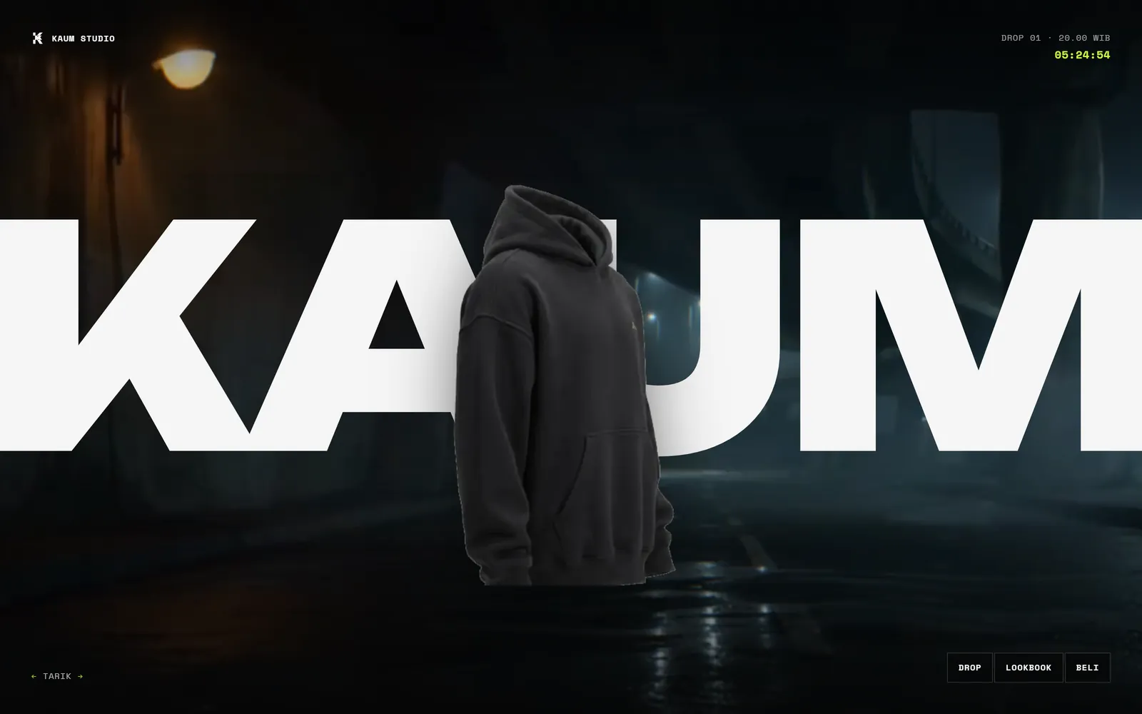 Halaman depan KAUM Studio: hoodie hitam melayang menembus wordmark raksasa di atas jalan basah pada malam hari